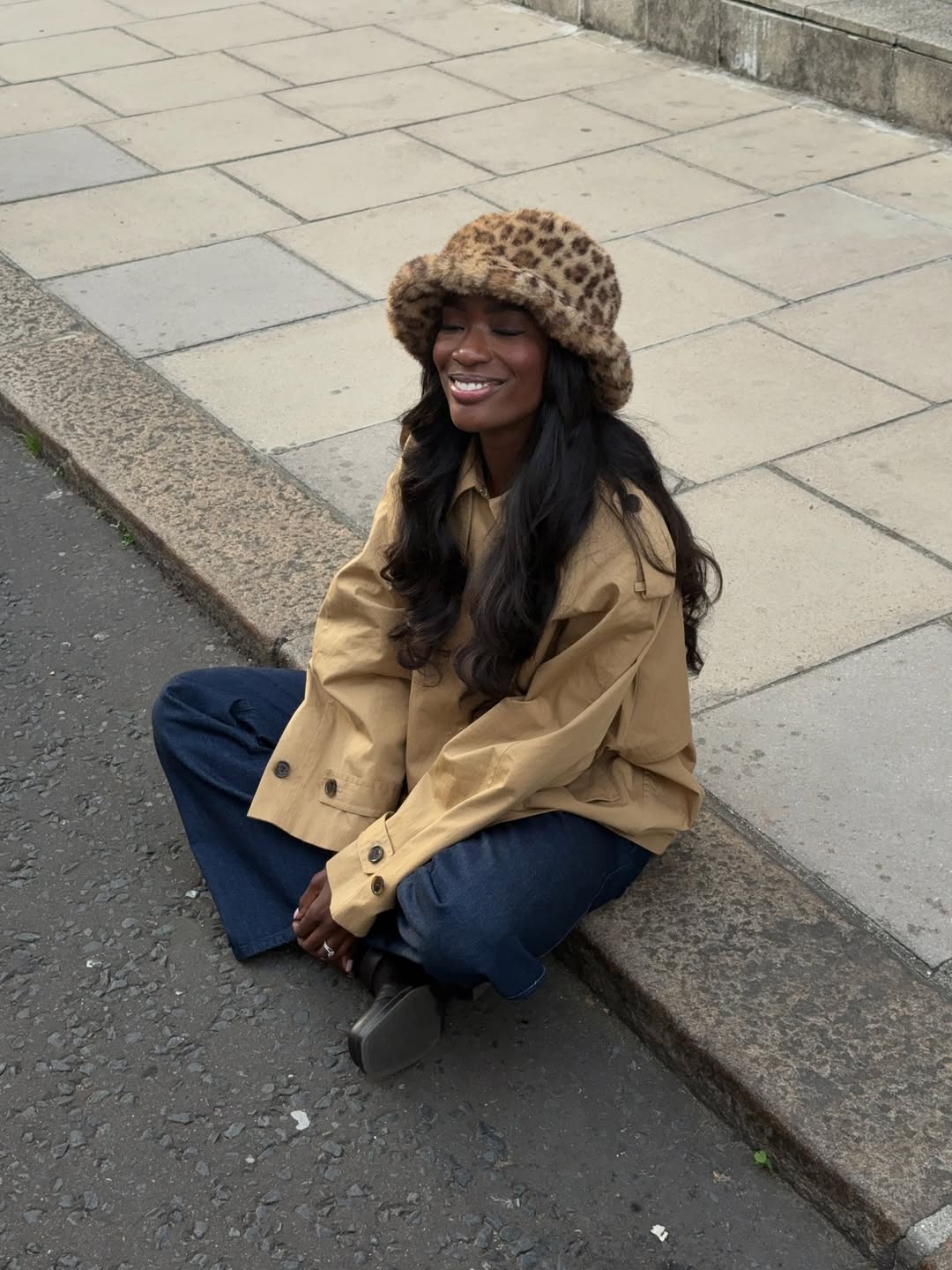 @_livmadeline wears jeans, black boots, trench coat, leopard print hat