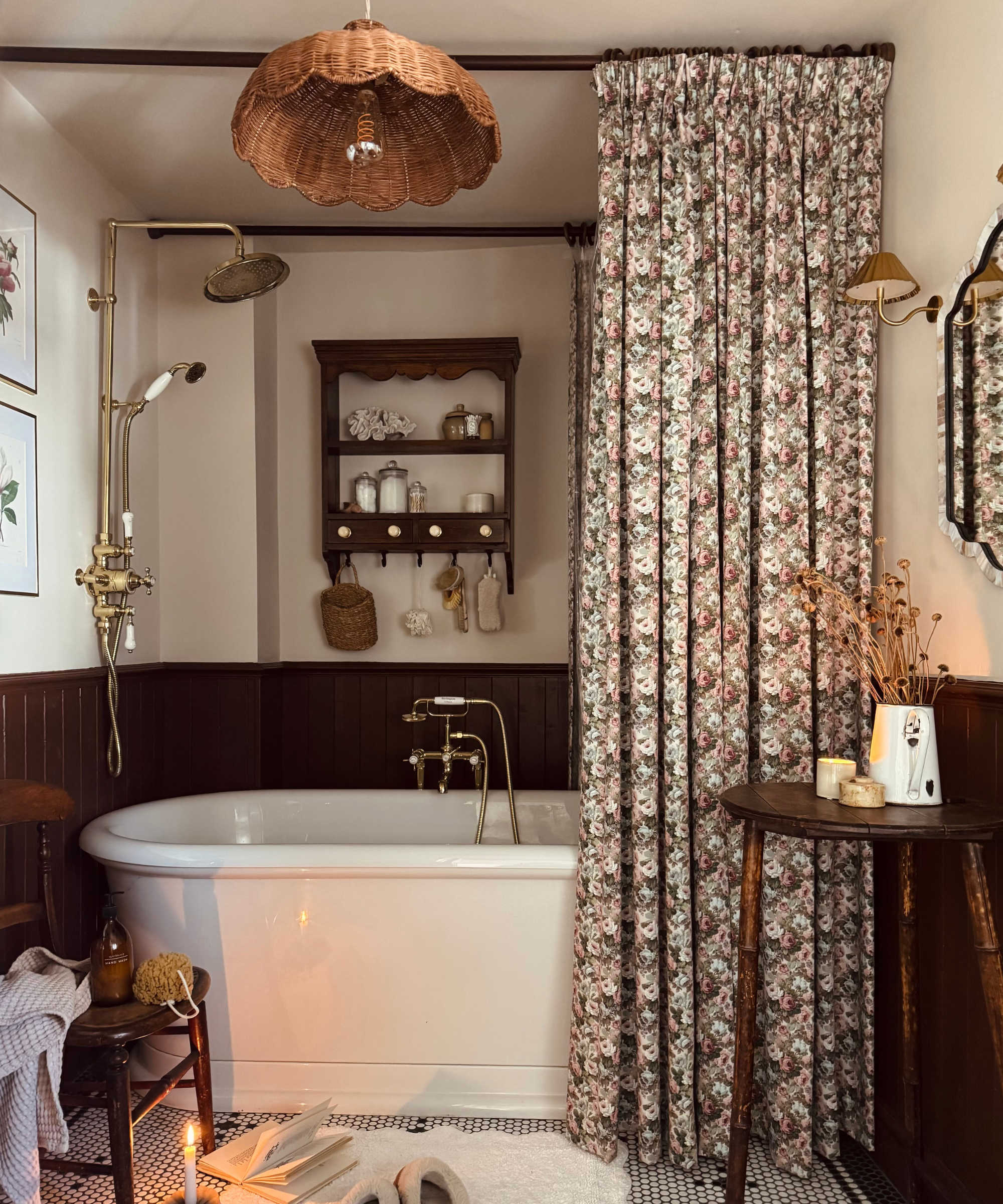 a bathroom with a floral printed shower curtain, a freestanding tub, a rattan ceiling light, a wooden stool, and a wooden wall shelf