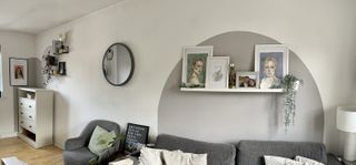 A panorama of a long wall with painted arches on and decorated with shelves, a mirror, plants, and prints.