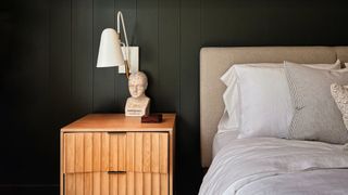 A bedroom with a dark wall and a statue next ot the bed illustrating the dark academia trend