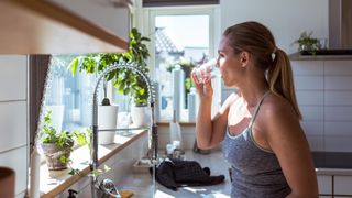 woman drinking a glass of water at her sink
