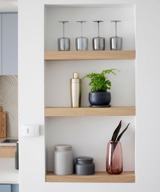 Open wooden shelving dress with decorative and culinary objects in painted white nook of kitchen/pantry space