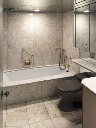 A dated bathroom with beige tiles and a built in bath