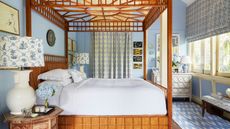 Blue bedroom with four poster bed, patterned blinds and curtains, chevron rug, white chest of drawers, and two white lamps either side of the bed with blue and white patterned lampshades.