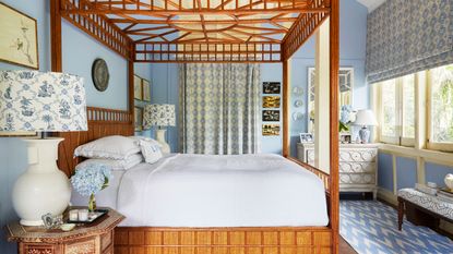 Blue bedroom with four poster bed, patterned blinds and curtains, chevron rug, white chest of drawers, and two white lamps either side of the bed with blue and white patterned lampshades.