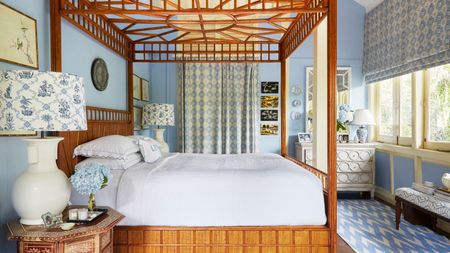 Blue bedroom with four poster bed, patterned blinds and curtains, chevron rug, white chest of drawers, and two white lamps either side of the bed with blue and white patterned lampshades.
