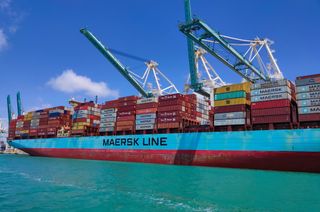 A large container ship filled with brightly coloured containers with the words Maersk Line displayed along its hull