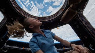 a female astronaut stares through a spacecraft window at earth