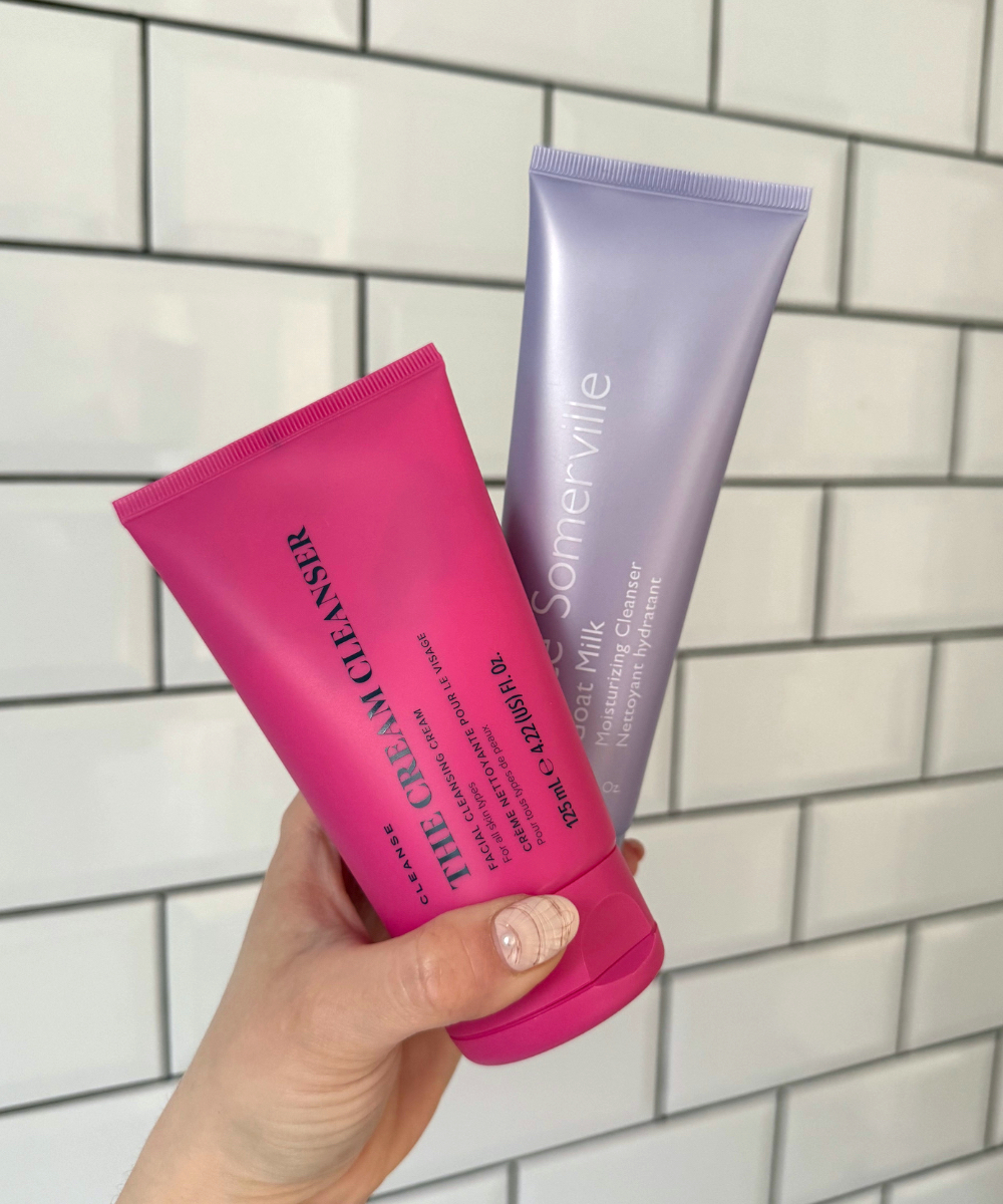 Handheld view of Skin Rocks The Cream Cleanser and Kate Somerville Goat Milk Moisturising Cleanser in front of a white tiled wall with black grouting