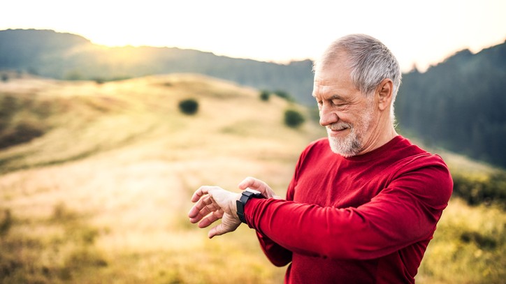 An active senior man outdoors in nature at sunrise, checking his running watch