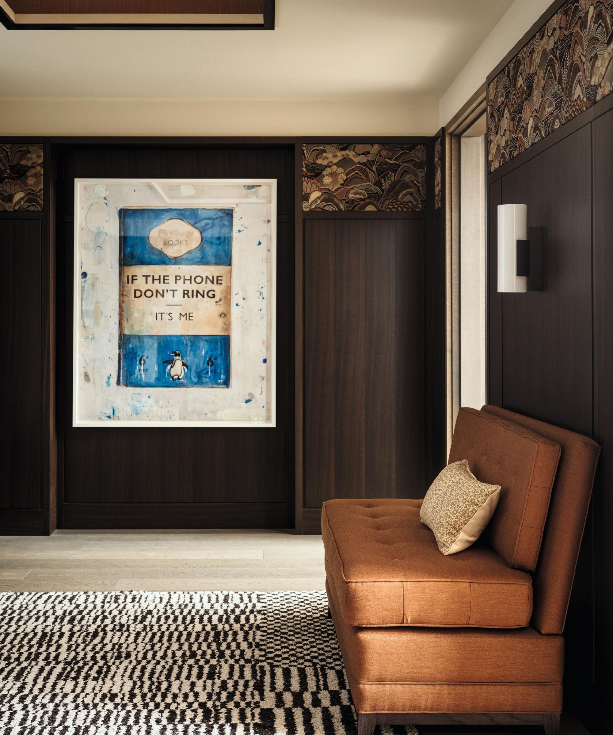 a dark wooden panelled entryway with a large Penguin book artowrk and an orange settee bench