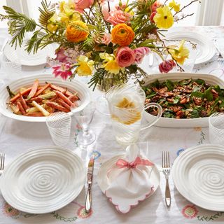 White table with serving bowls of food surrounded by plates, cutlery and glasses