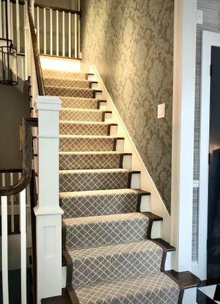 Staircase with brown geometric runner and patterned wallpaper