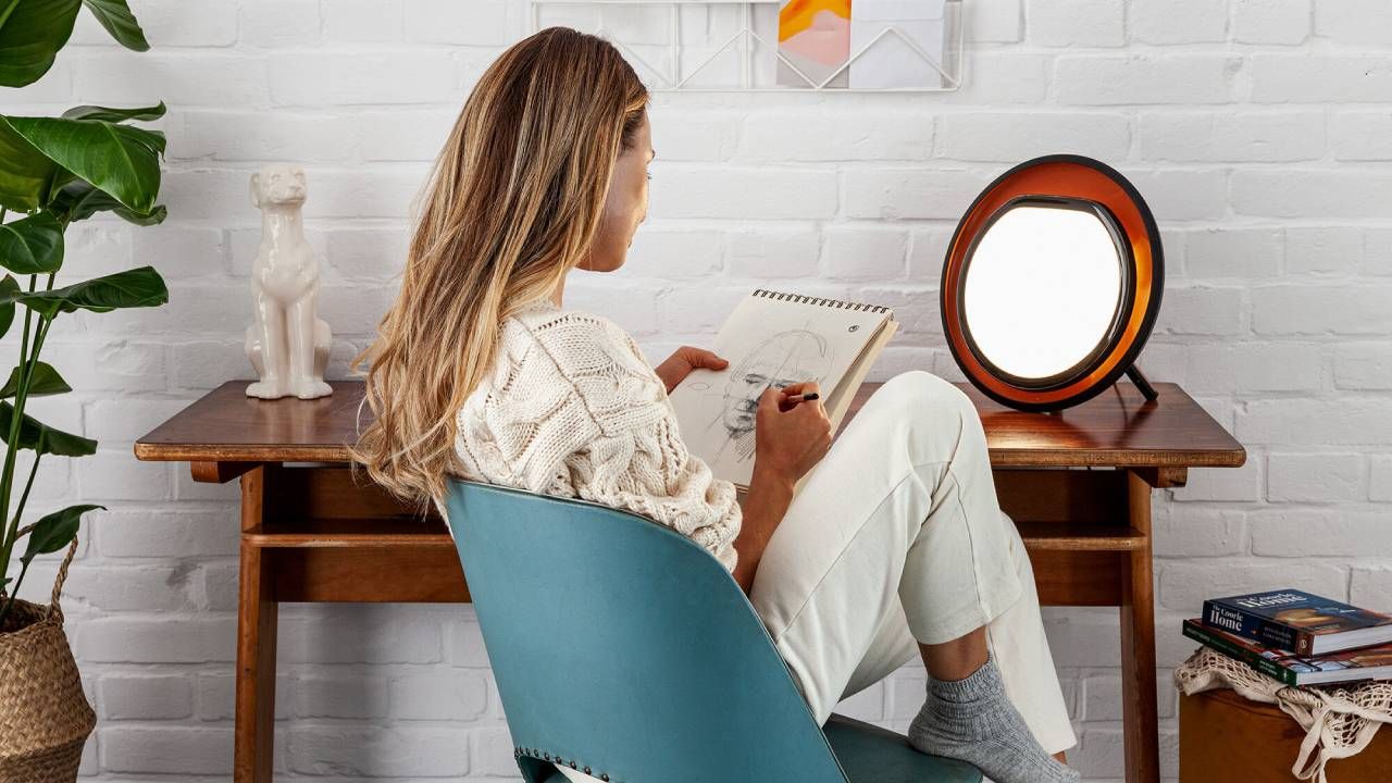 Woman sitting in front of a Lumie SAD lamp while drawing