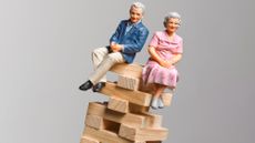 Miniature figurines of an elderly couple sitting on top of a toppling stack of blocks