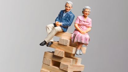 Miniature figurines of an elderly couple sitting on top of a toppling stack of blocks