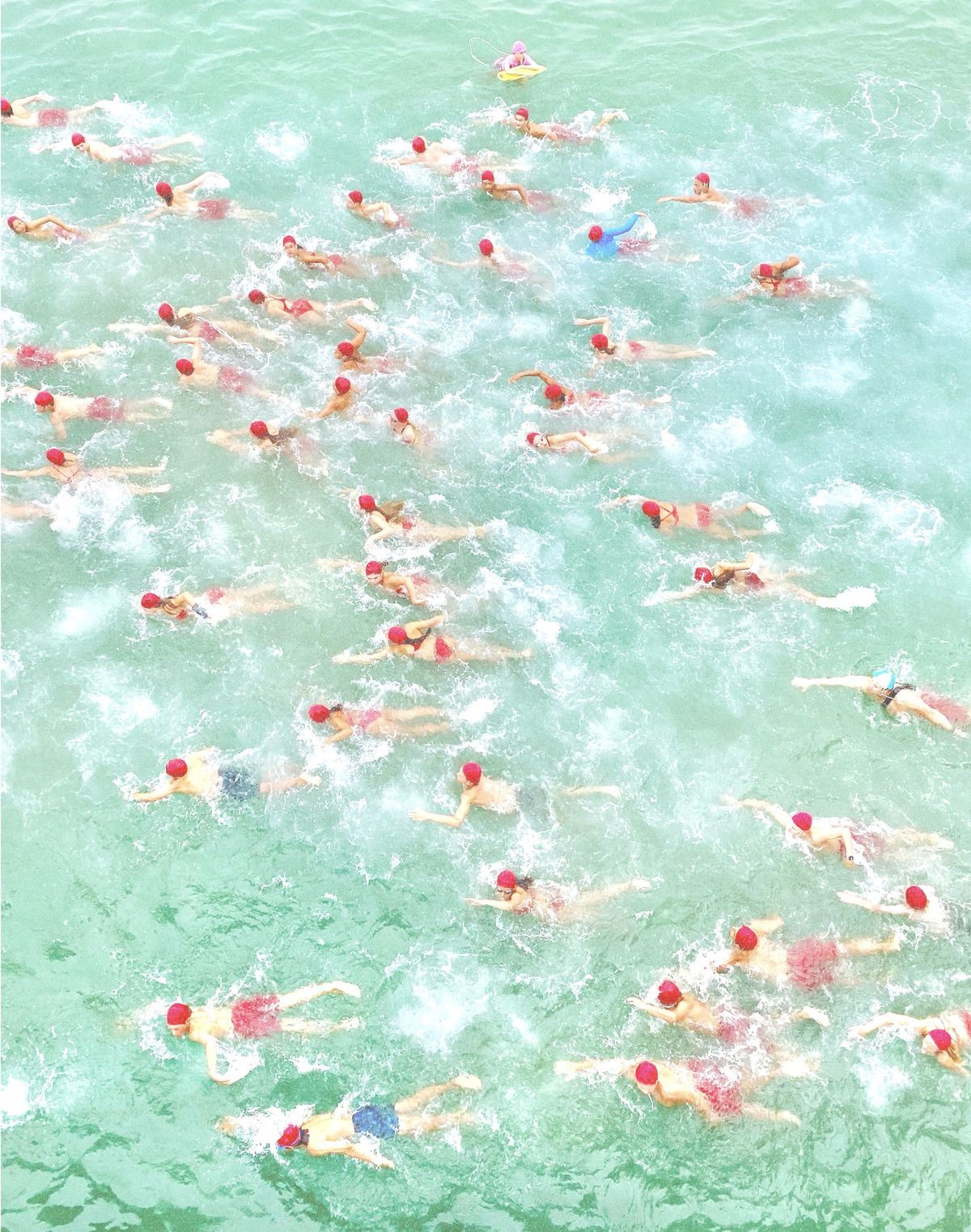 A group of swimmers in red caps in a green river