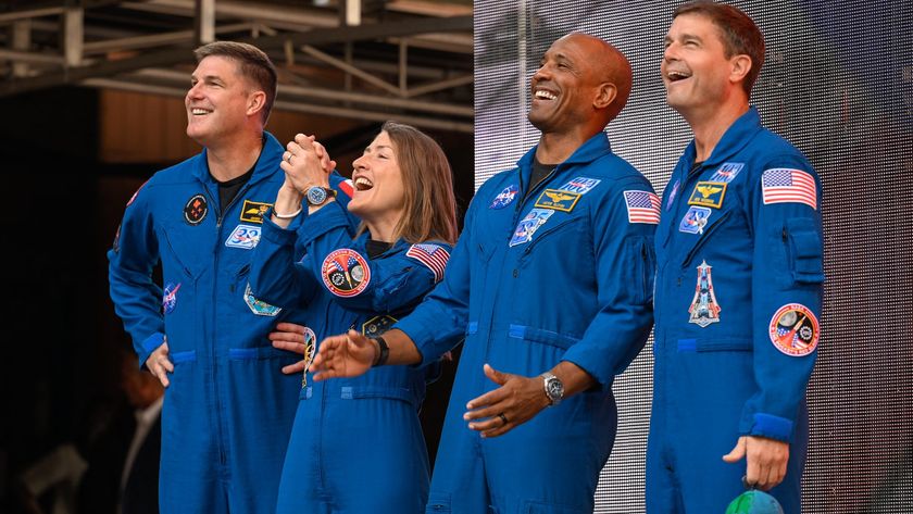 four people in blue flight suits stand on a stage in an amphitheater surrounded by red stone cliffs