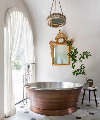 Neutral bathroom with curved window with sheer drapes and a round copper bath tub