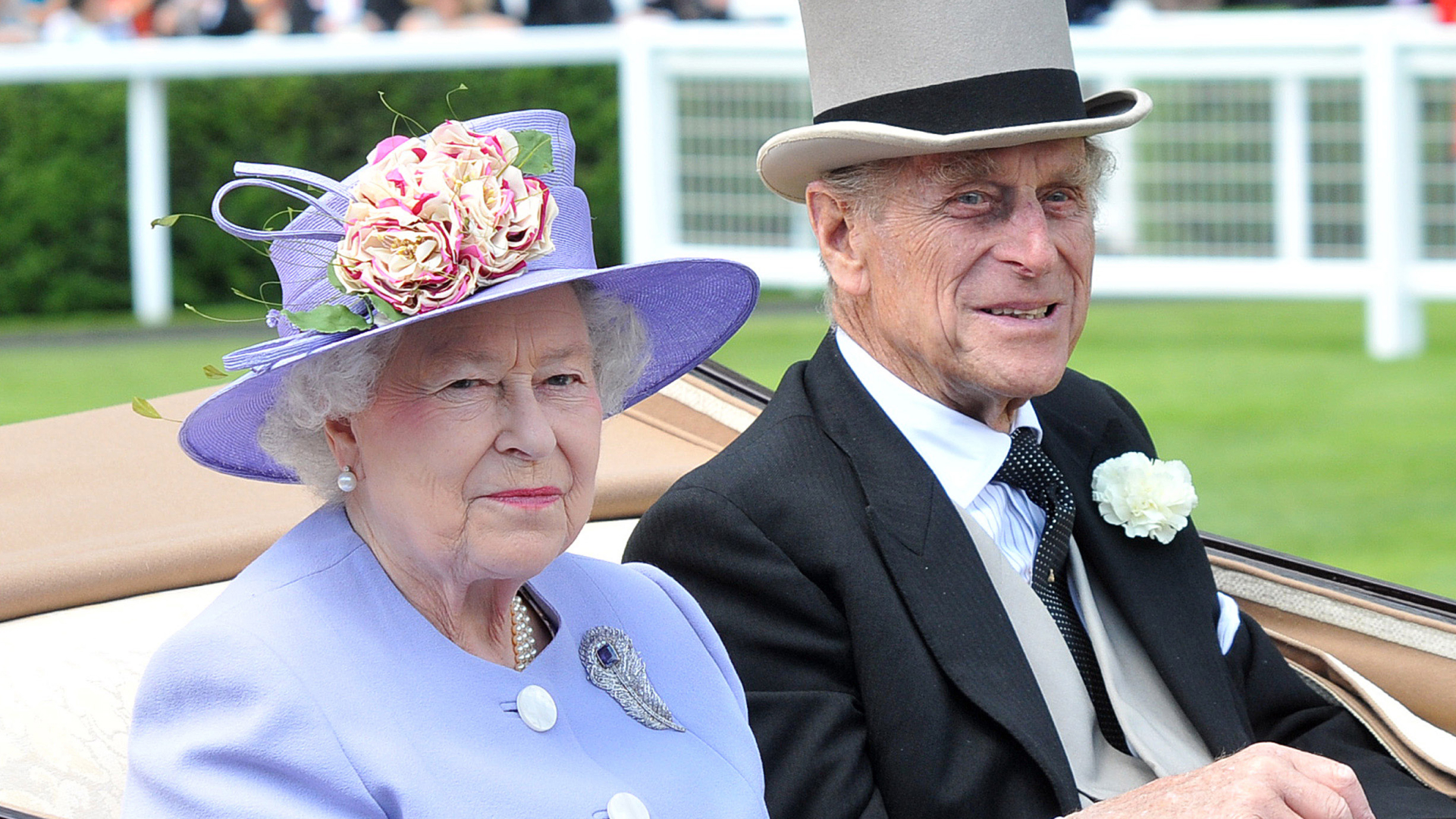 Queen Elizabeth wearing a lilac hat and coat and sitting next to Prince Philip who wears a top hat