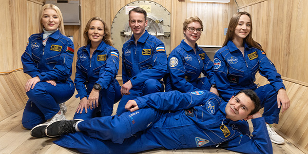 six people in blue flight suits pose for a portrait