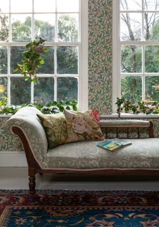 Victorian chaise longue with floral print and needlepoint cushions by the bedroom window with festive foliage and leafy wallpaper design