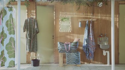 A wood panelled wall and bench with patterned towels and bags handing on pegs