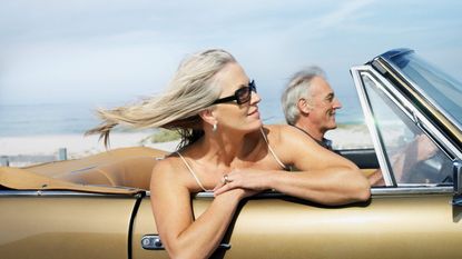 A gray-haired couple enjoy a ride in a convertible with the top down.