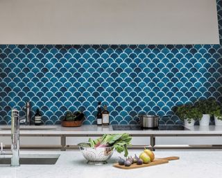 Blue scallop shaped tiling on kitchen backsplash with kitchen sink, faucet and fresh produce on worksurface