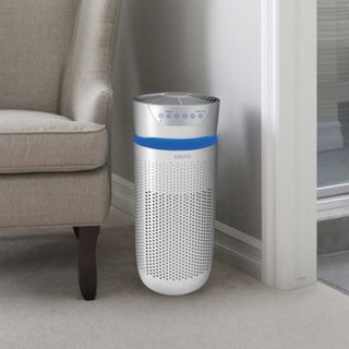 HoMedics TotalClean 5-in-1 Tower Air Purifier in white next to cream armchair