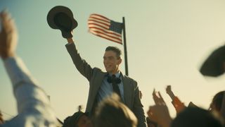 Cillian Murphy's Robert J Oppenheimer holds his hat and smiles at an assembled crowd in Christopher Nolan's Oppenheimer movie
