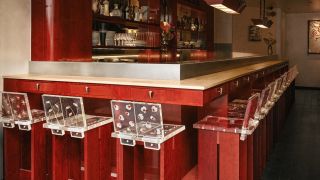 A red-painted wood and chrome bar of a restaurant, decorated with tall, geometrically cut wooden stools with flower-decorated resin backs.