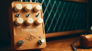 A photo of the Universal Audio Enigmatic ’82 Overdrive Special Amp pedal in shadow alongside a vintage Dumble amplifier and an electric guitar