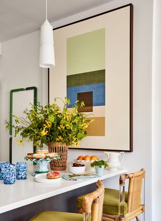 dining table with a bouquet of flowers with green countertop stools and a large artwork behind