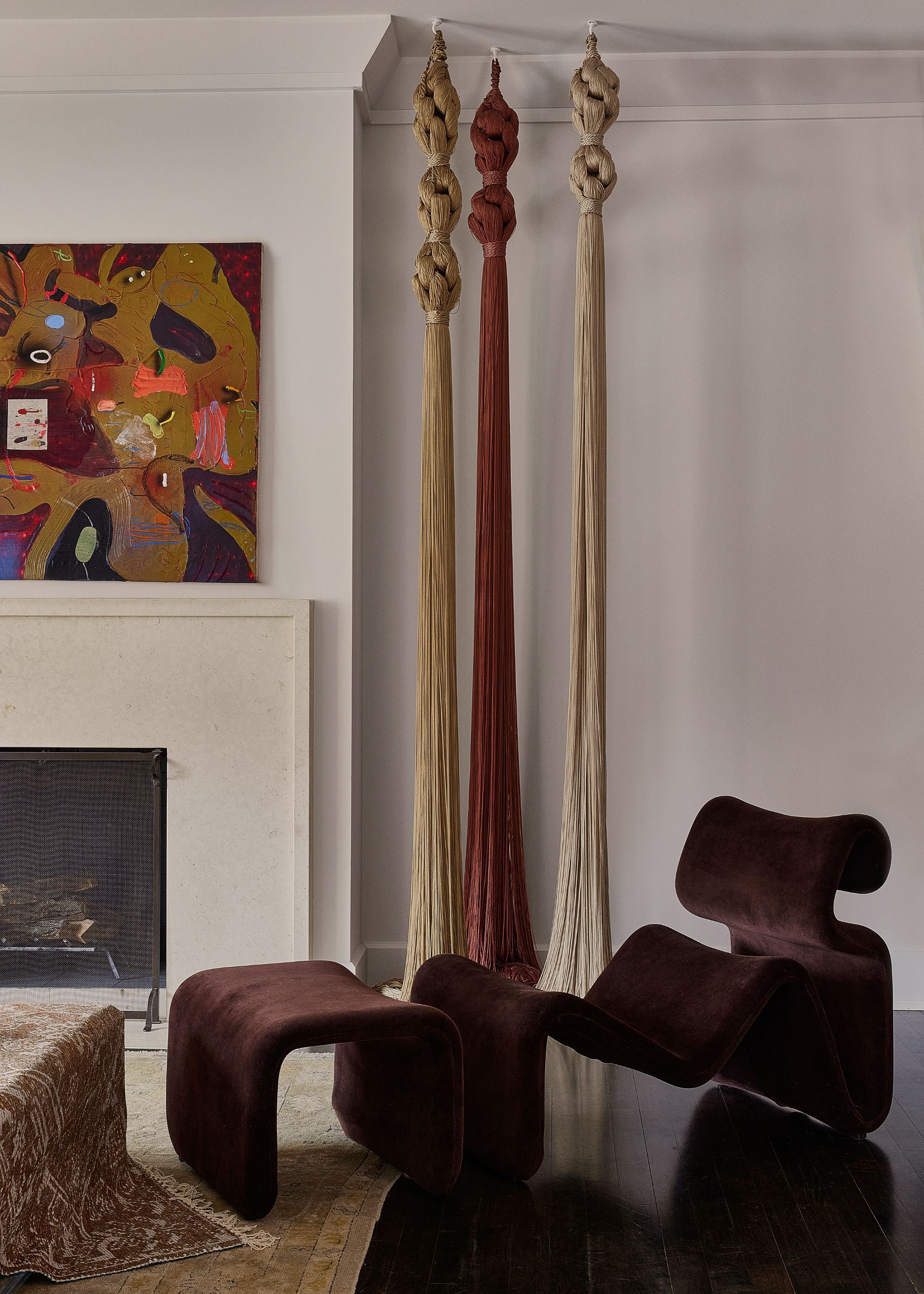 A corner in a living room with long hanging tassels, and a plum accent chair