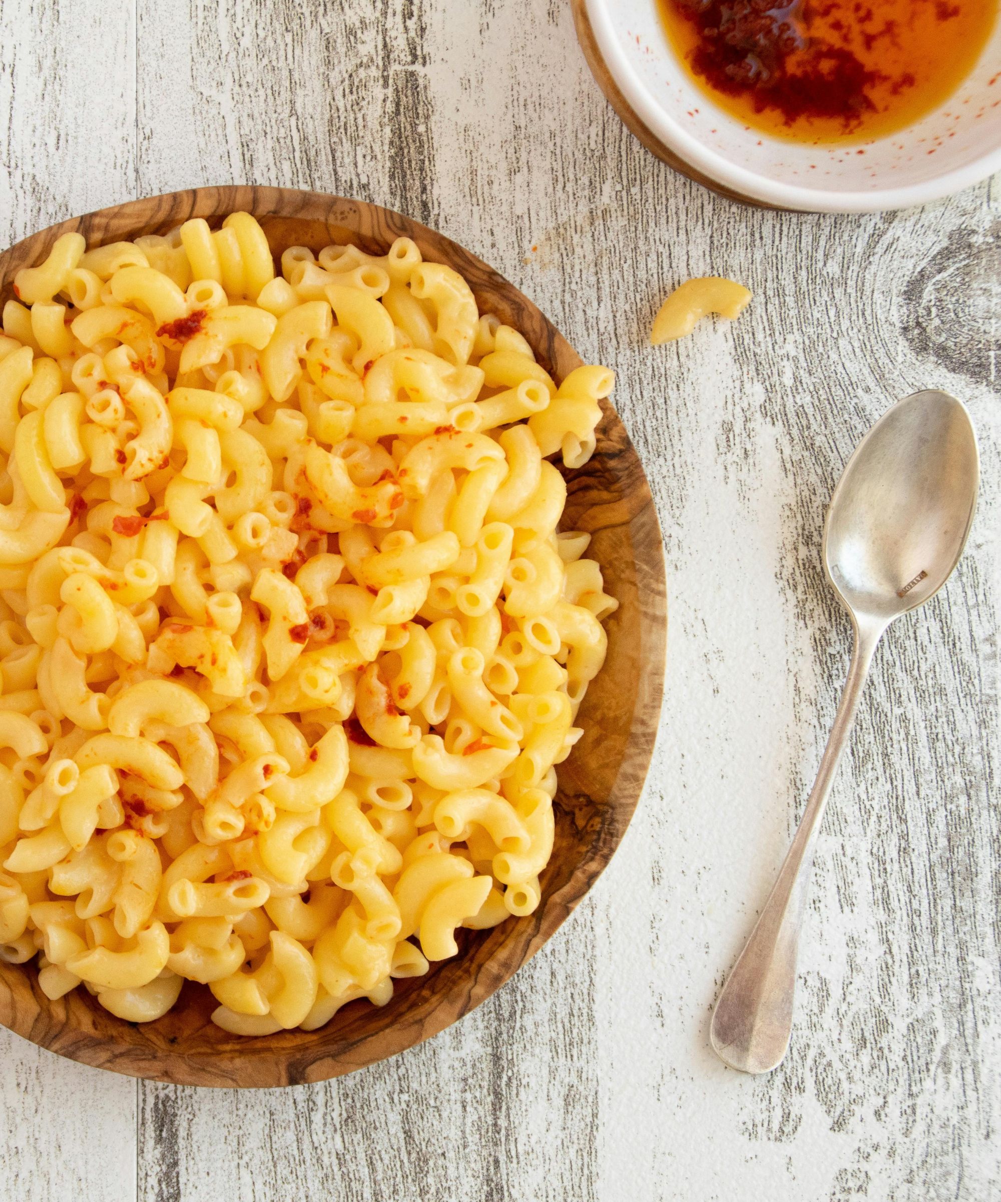 Wooden bowl of macaroni next to a silver spoon