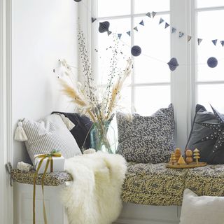 Window seat covered in cushions and rugs, with paper string decorations hanging above