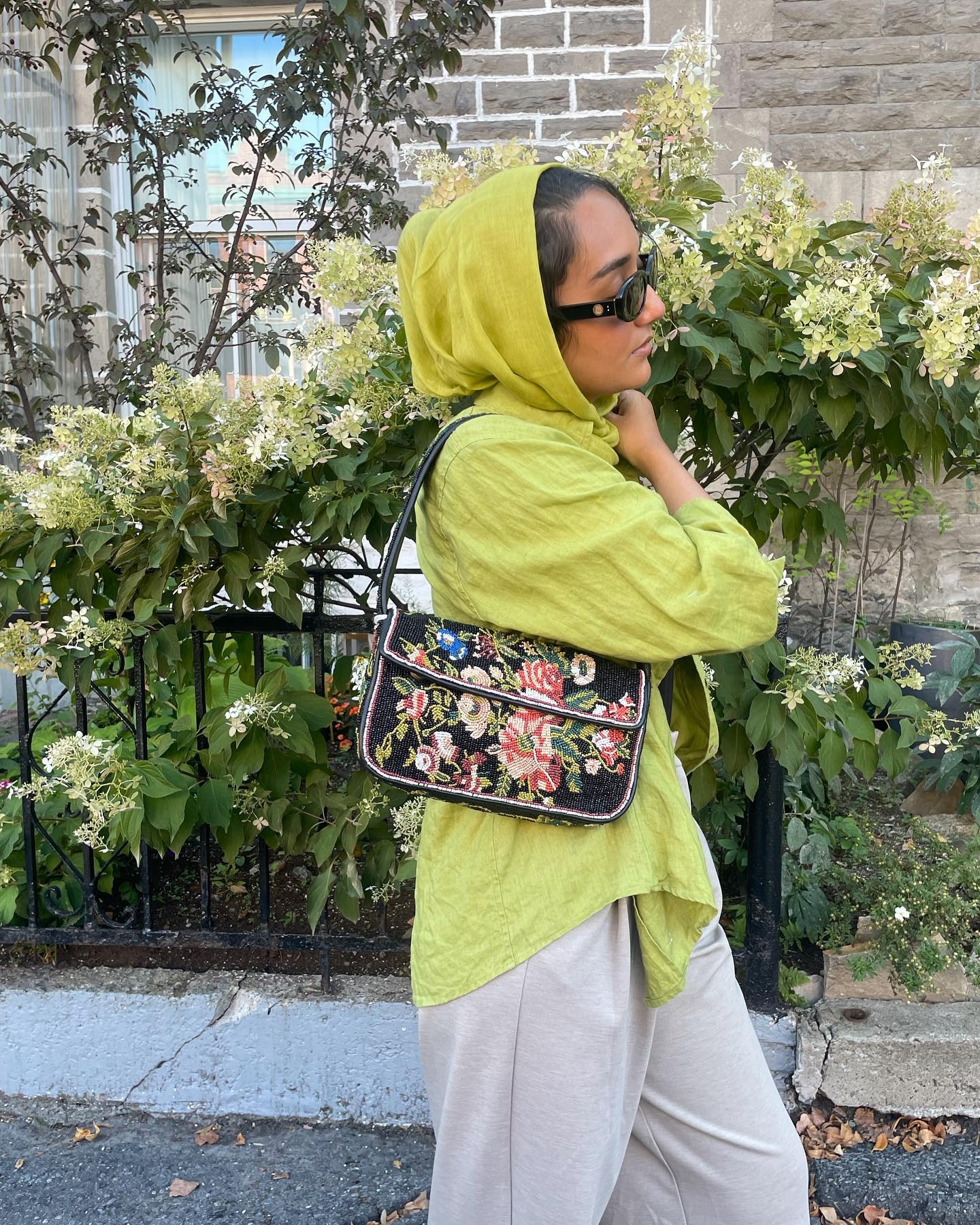 @thatgirlyusra wearing a green top, white pants, and a beaded Staud bag.