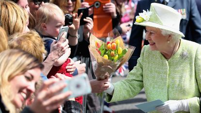 Queen Elizabeth wearing a green coat and taking a bouquet from a member of the public