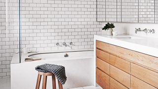 white bathroom with metro tiles with large wooden storage unit under the sink and mirrored wall cabinets showing how to avoid bathroom design mistakes of insufficient storage