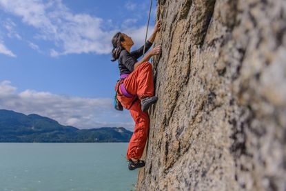 A strong woman is climbing a steep rock face while roped in.