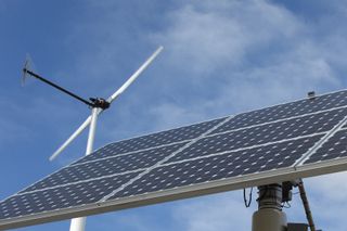 Solar panels with wind turbines in the background