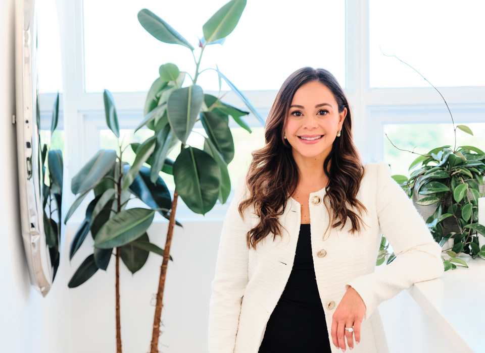 a white woman with dark hair in a white coat surrounded by plants