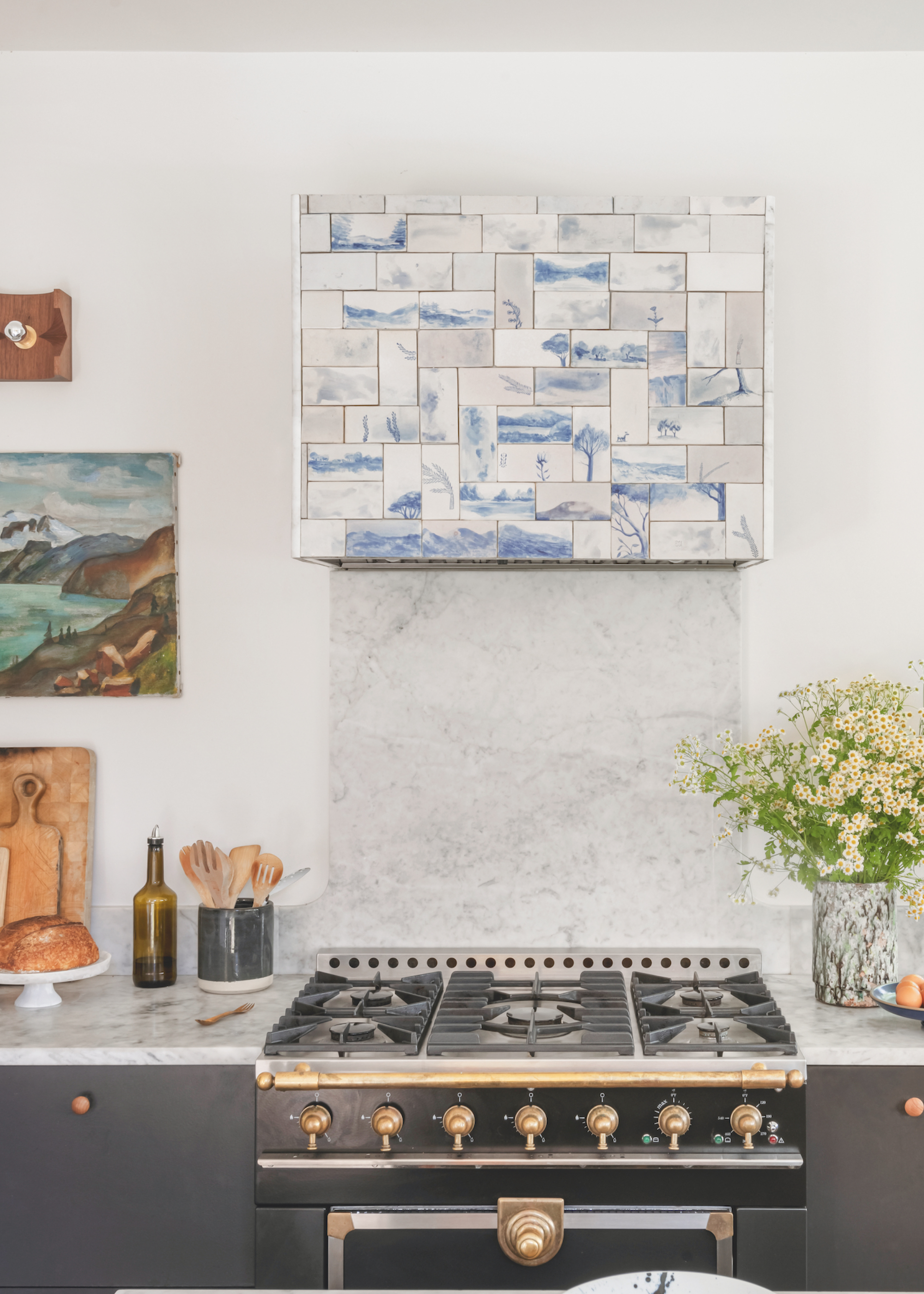 A white walled kitchen with a view of the hob and oven. The island, worktops and backsplash are all white marble and there is a blue and marble tile over the extractor above the hob.