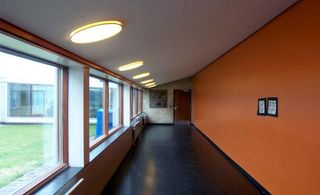 School corridor with windows all along the left side looking out to courtyard and bright orange wall to the right.