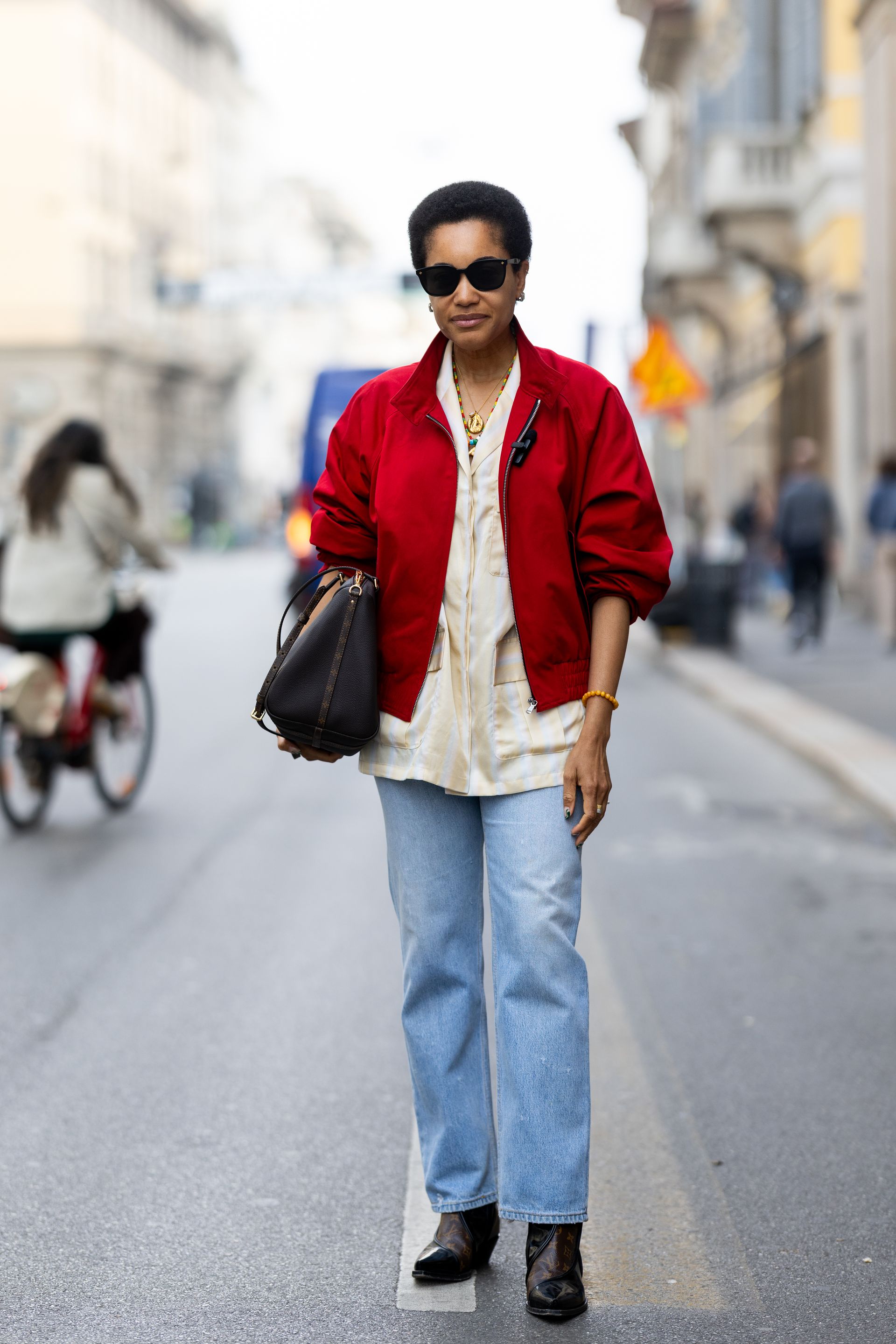 A woman wears a red jacket, white top, light-wash jeans, and brown boots.