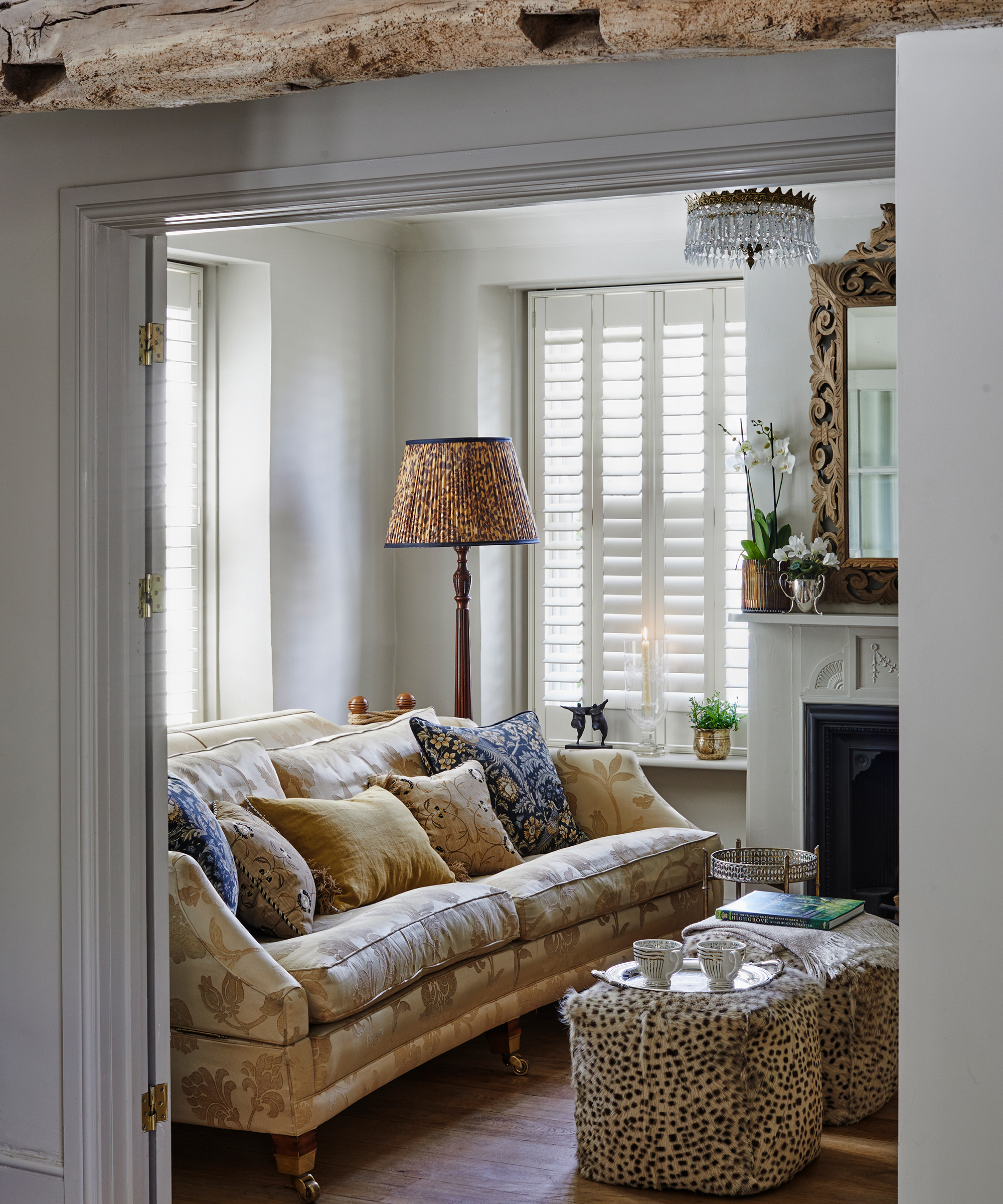 View through to living room in a period home with window shutters, gold sofa and animal print pouffs