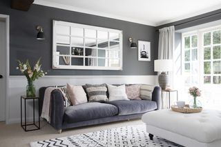 Dark grey living room with grey velvet sofa, black and white boho rug, white studded ottoman and white mirror
