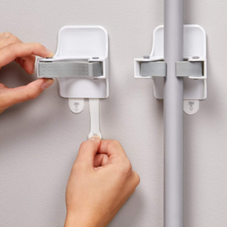 A person using Command hooks to store mops and brooms.