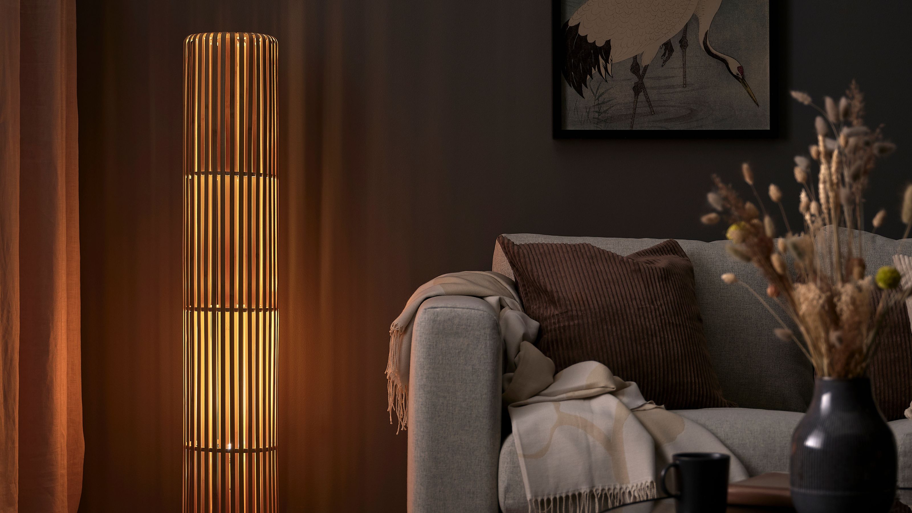 IKEA VARPTROSS Floor Lamp next to gray sofa with cushion and throw, artwork hung on wall behind, and a coffee table styled with vase of dried flowers
